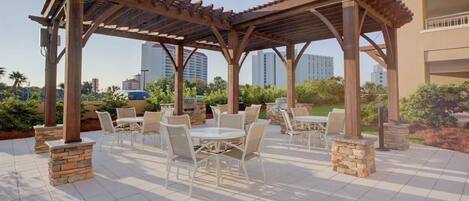 An outdoor patio with a pergola, stone pillars, and white outdoor furniture.