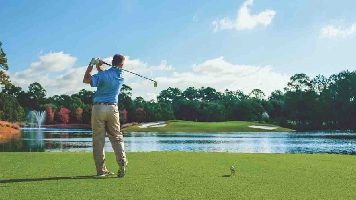En golfspiller på en golfbane med et vandhul og træer i baggrunden.
