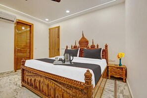 A bedroom with a large bed, wooden headboard, a nightstand with a vase of flowers, and a wall-mounted air conditioning unit. - Hotel Right Palace And Banquet (New Delhi)