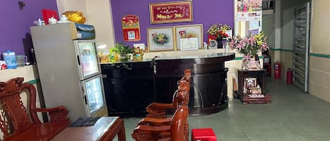 Une salle d’attente avec un mur violet, des meubles en bois, un réfrigérateur et un comptoir où sont exposés divers objets.