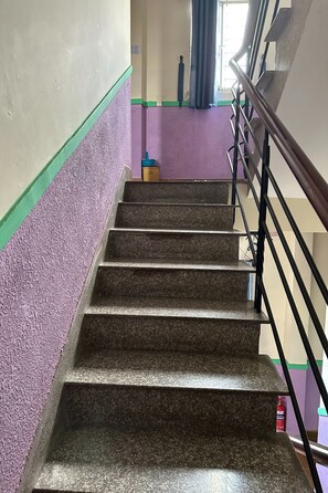 Eine Treppe mit Handlauf, die zu einer Zwischenebene führt, auf der sich ein Feuerlöscher und ein blaues Objekt befinden.