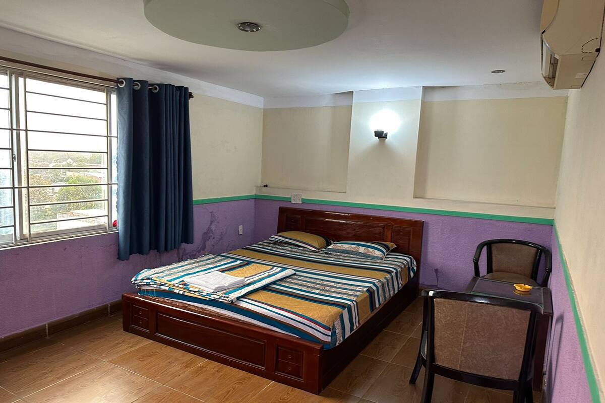 Ein Schlafzimmer mit einem hölzernen Bett, einem Sessel, einem Fenster mit Vorhängen und einer Wandleuchte.