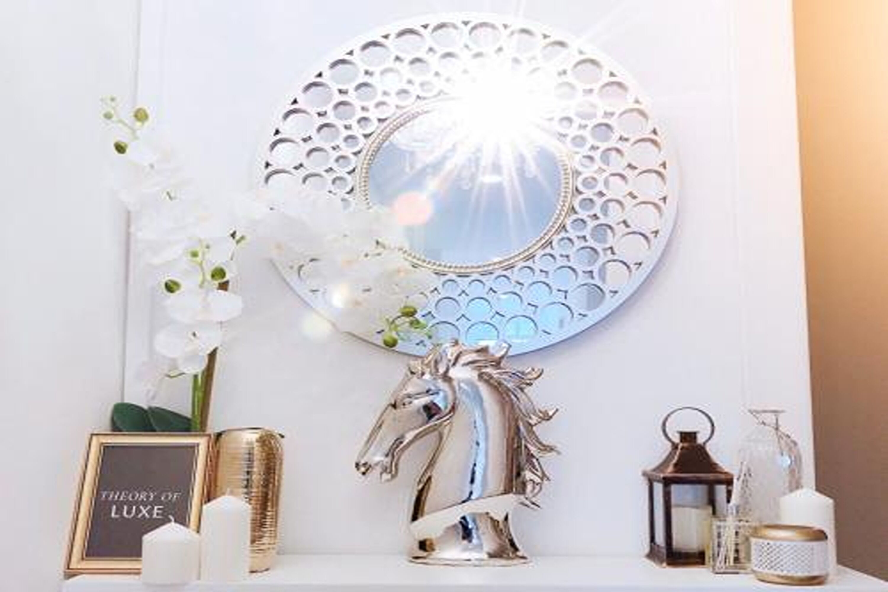 A decorative wall piece with a circular design, a framed sign, a metallic horse sculpture, and various small decorative items on a white surface.