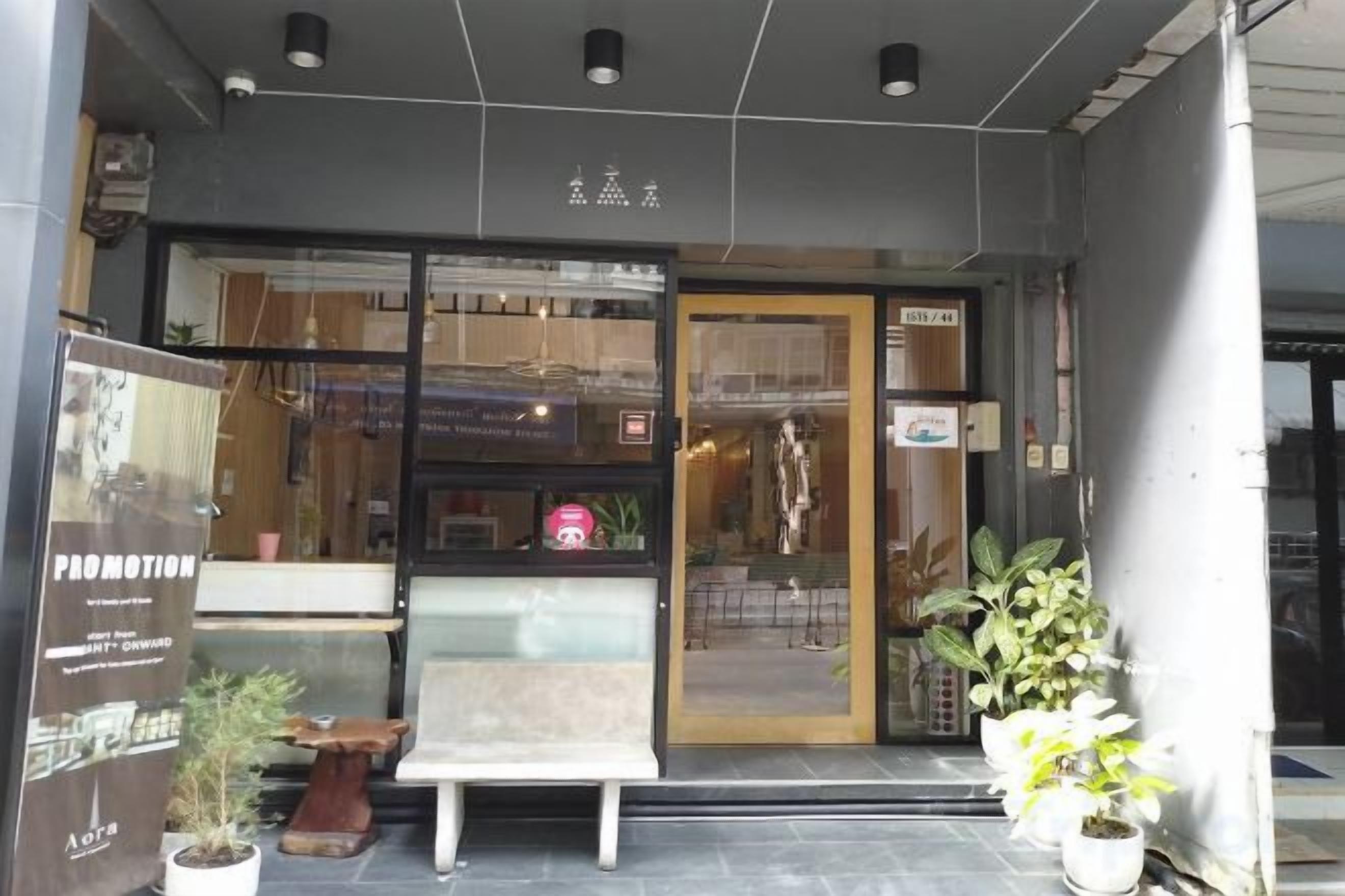 Een winkel met een glazen deur, planten in potten en een bankje ervoor.