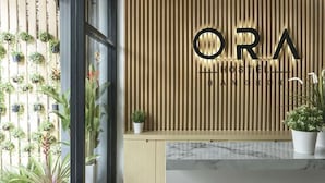 Un comptoir d’accueil avec un mur composé de lattes de bois et l’inscription « ORA HOSTEL BANGKOK » illuminée.