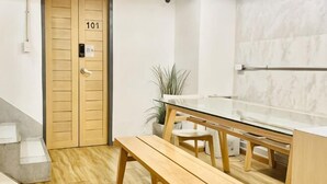 Une pièce avec une porte en bois portant l’inscription « 101 », une table en verre, des bancs en bois, une plante en pot et un mur en marbre.