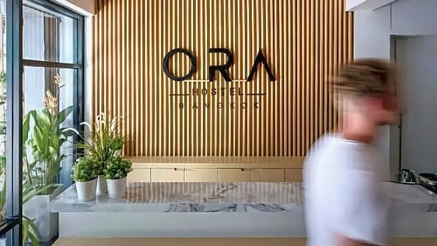 Un intérieur moderne avec un mur composé de lattes de bois et l’inscription « ORA HOSTEL », qui indique le nom de l’établissement.