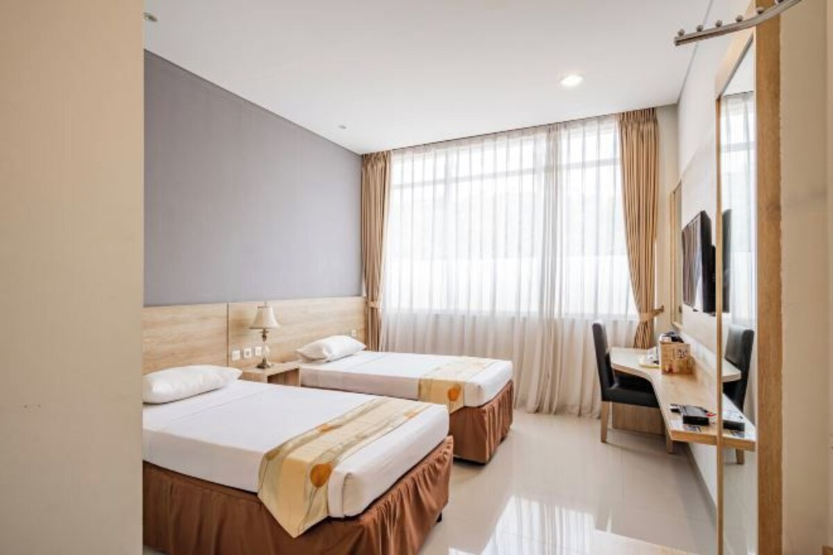 A hotel room with two beds, a desk, a chair, and a large mirror.