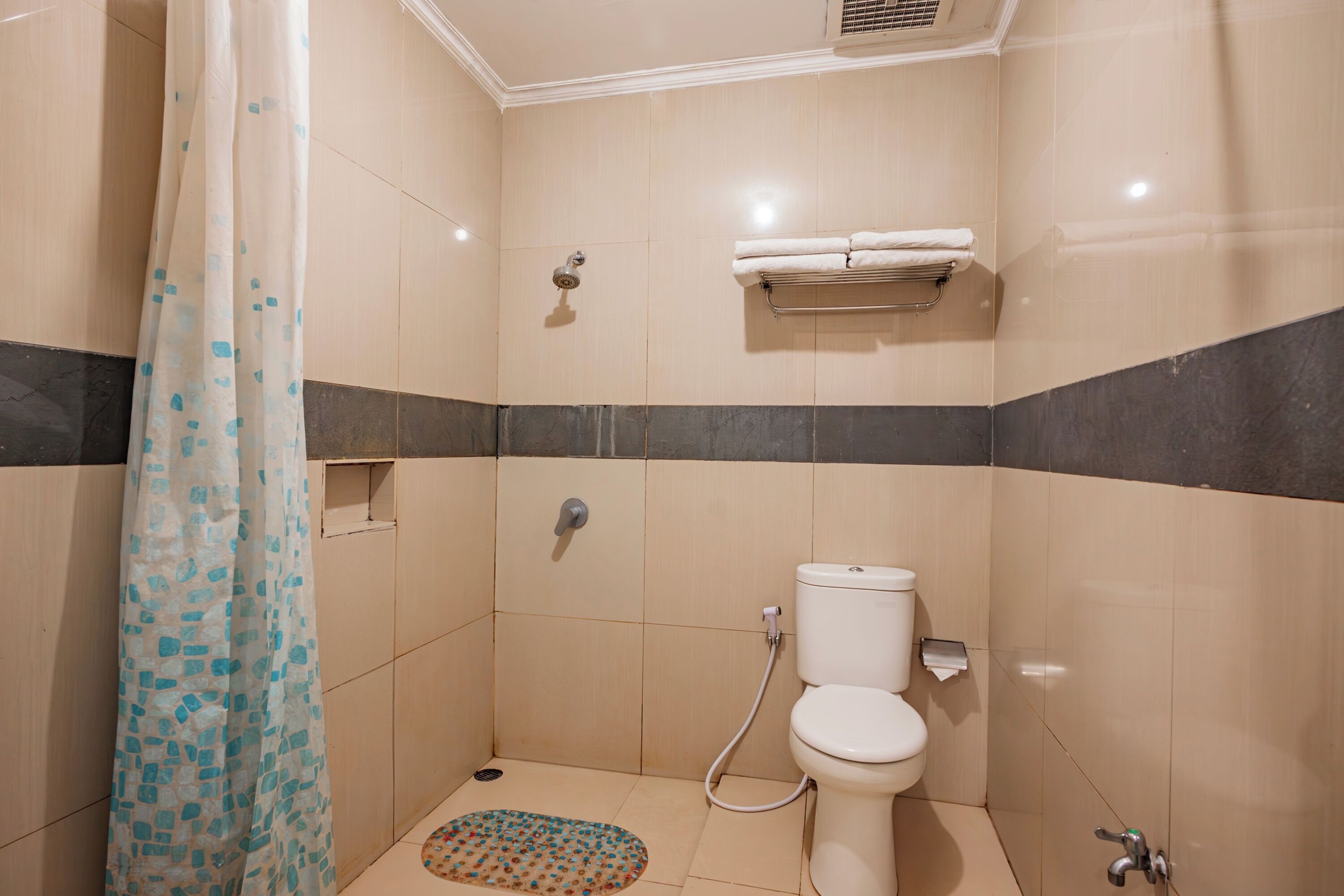 A small, tiled bathroom with a shower curtain, a toilet, and a towel rack.