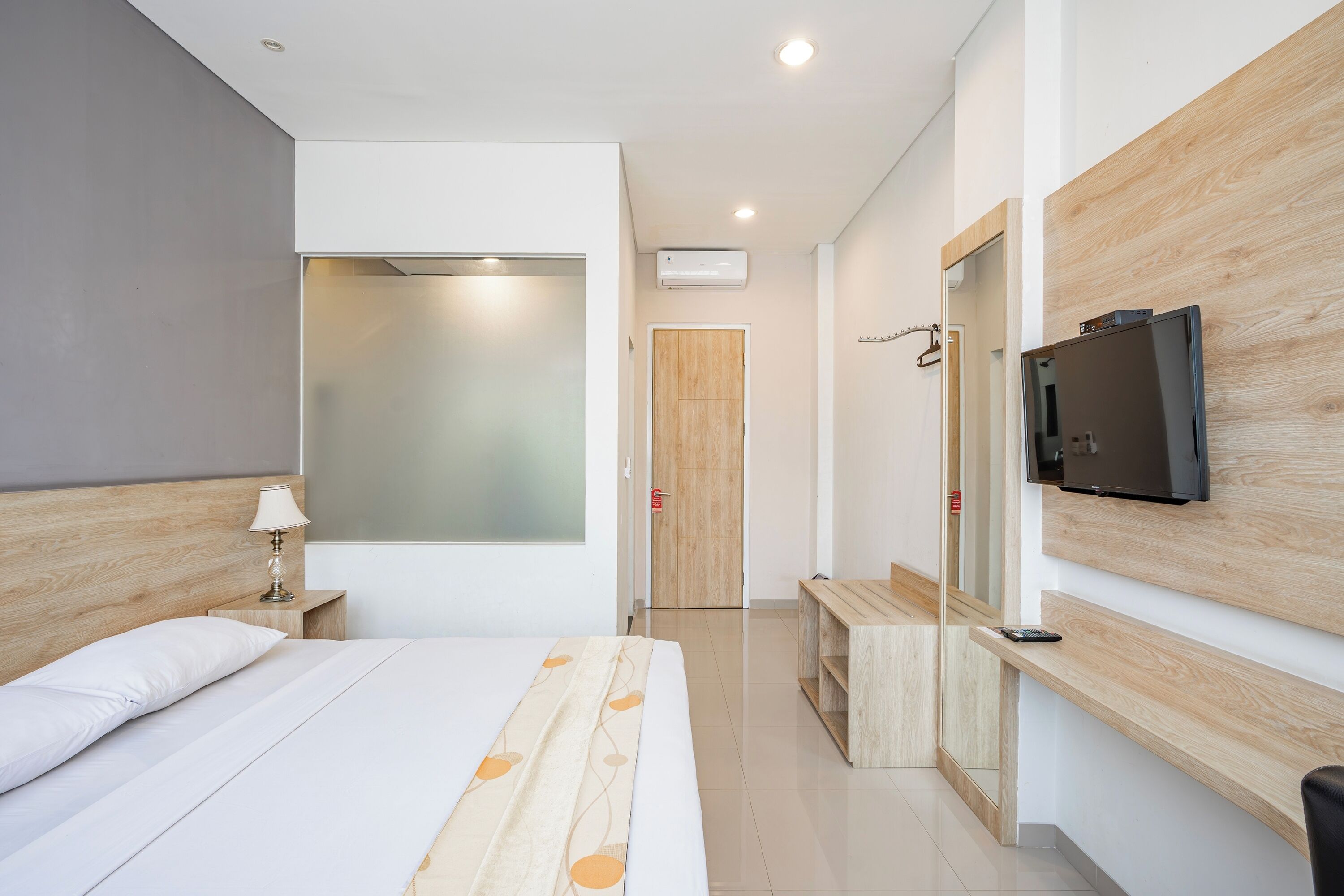 Una habitación de hotel moderna con cama, mesita de noche, lámpara, televisor y espejo.