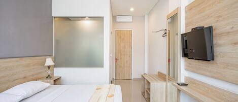 Una habitación de hotel moderna con cama, mesita de noche, lámpara, televisor y espejo.