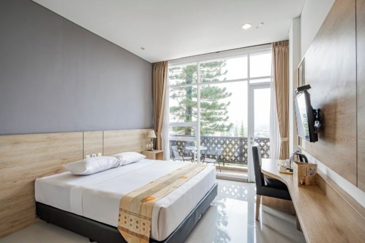 A modern hotel room with a large bed, a desk, and a balcony with outdoor seating.