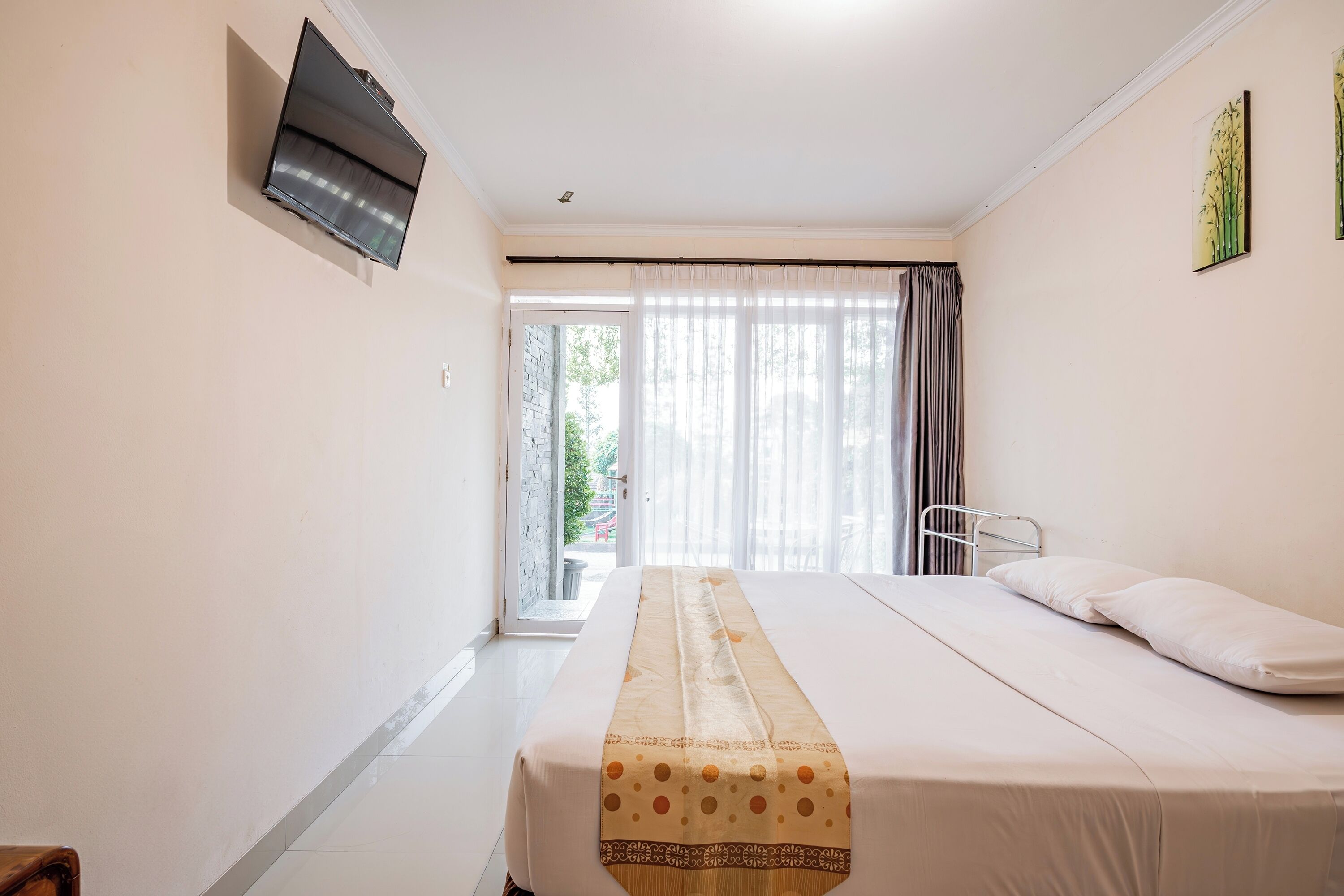 Habitación de hotel con cama, televisor montado en la pared, ventana con cortinas y vistas al exterior.