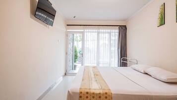 Habitación de hotel con cama, televisor montado en la pared, ventana con cortinas y vistas al exterior.