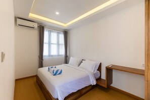 Habitación de hotel con cama, un banco de madera, equipo de aire acondicionado y una ventana con cortinas.