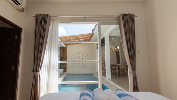 A hotel room with a bed, towels, a view of a pool, and a sliding door leading to a balcony. - B'Sheika Jimbaran (Jimbaran)