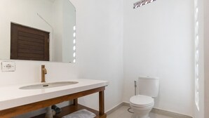 A bathroom with a white sink, a mirror, a wooden vanity, a toilet, and a shower area. - B'Sheika Jimbaran (Jimbaran)
