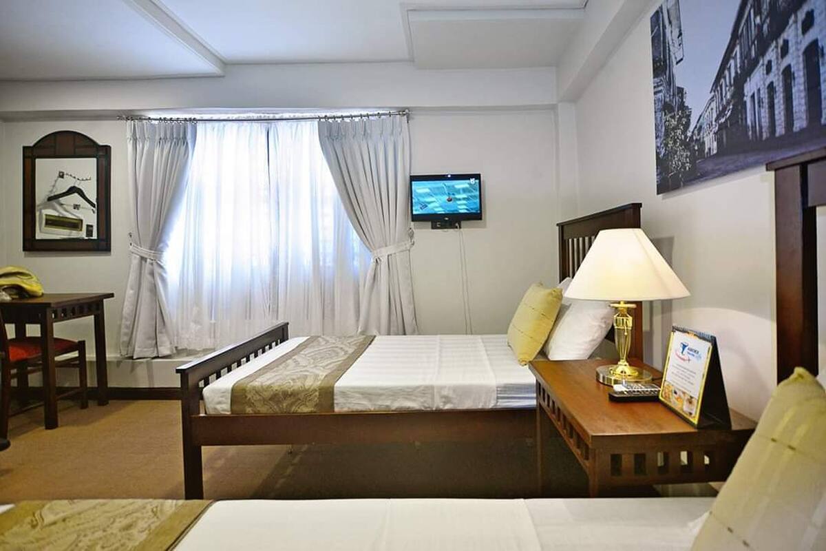 A hotel room with a bed, a desk, a chair, a television, and a window with curtains.