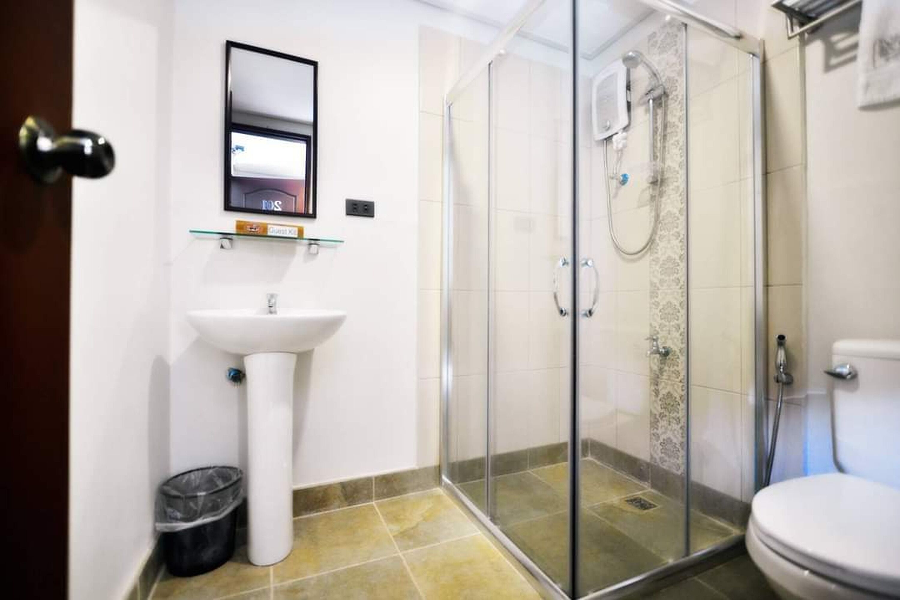 Een moderne badkamer met een douche met glazen wand, een wastafel op voetstuk en een toilet.