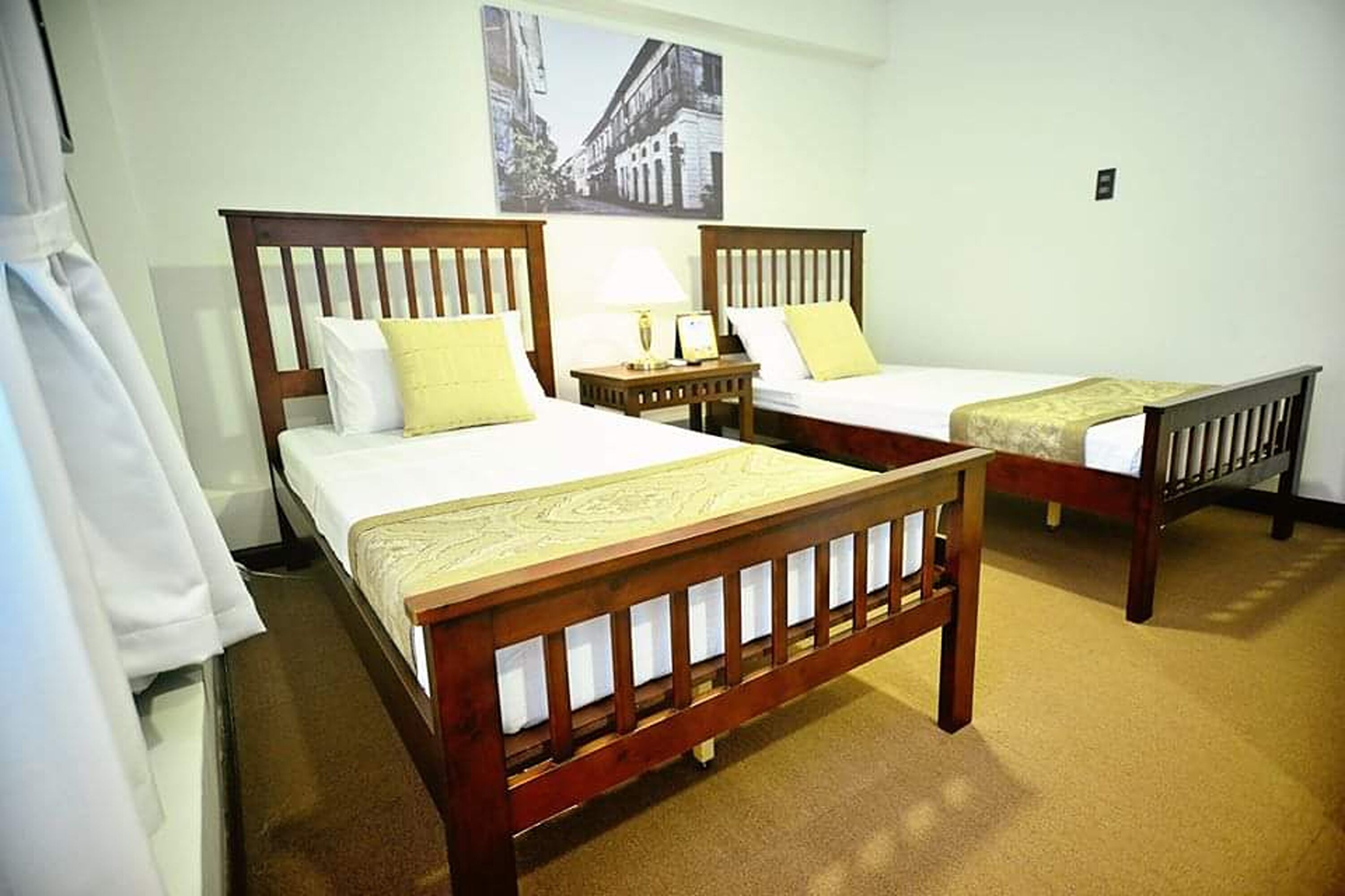 A hotel room with two wooden beds, a nightstand, and a wall-mounted picture.