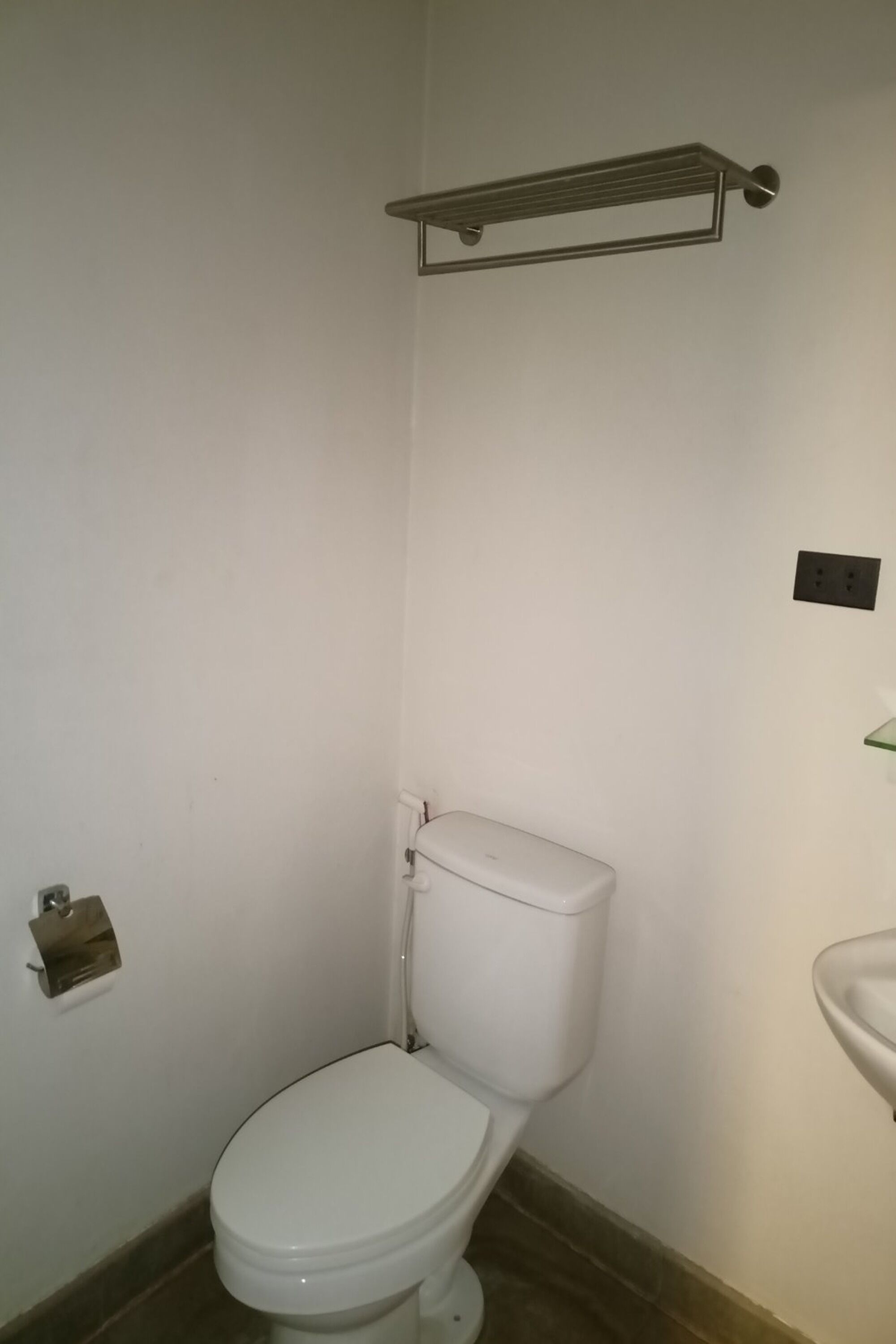 Ein kleines, sauberes Badezimmer mit einer weißen Toilette, einem Regal darüber und einem Waschbecken auf der rechten Seite.