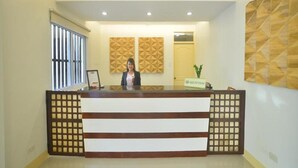 A reception desk with a nameplate, a window with vertical blinds, and decorative wall panels. - Metro Vigan Inn - Annex (Vigan)
