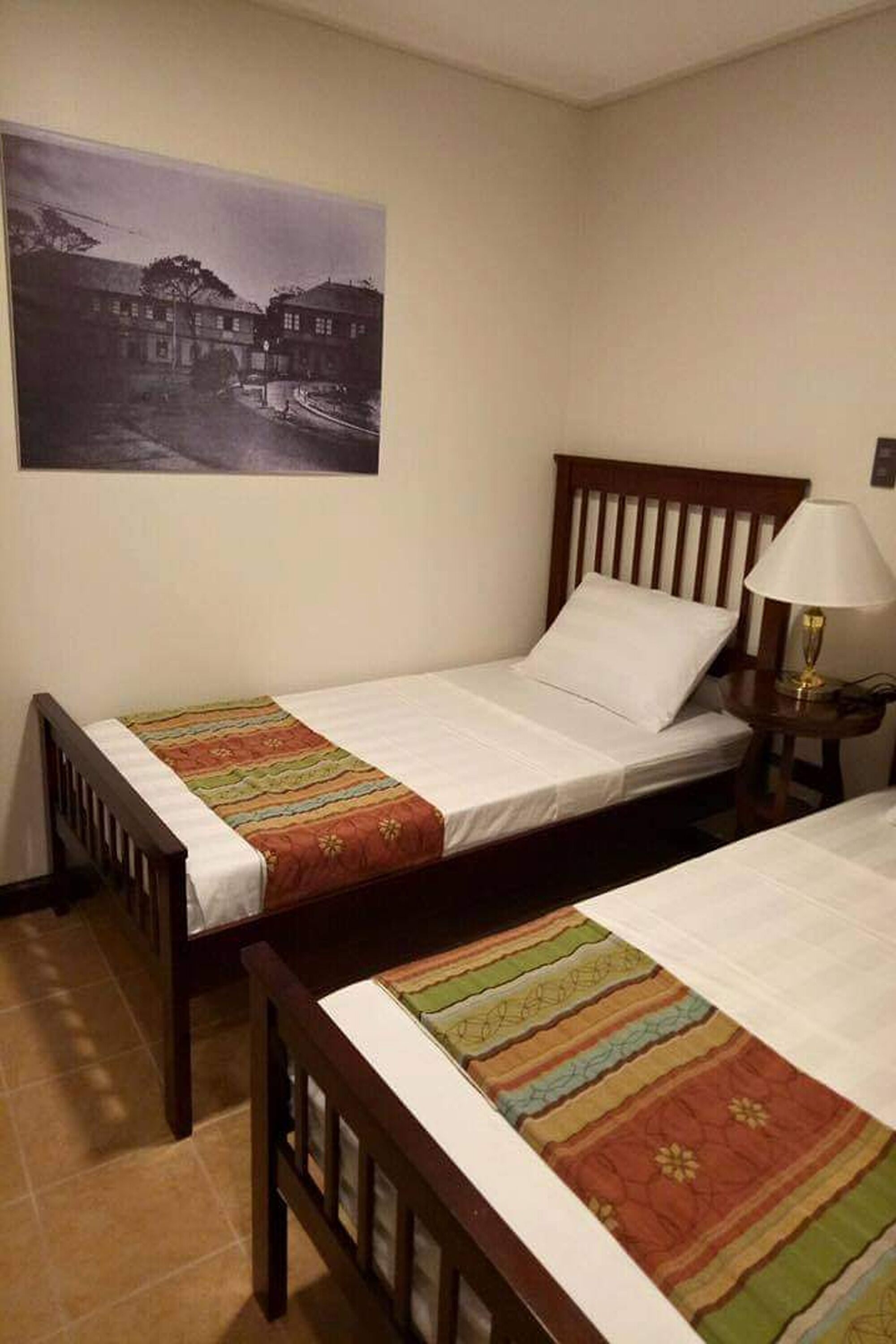 Una habitación con dos camas individuales, una mesita de noche con lámpara y un cuadro en la pared.