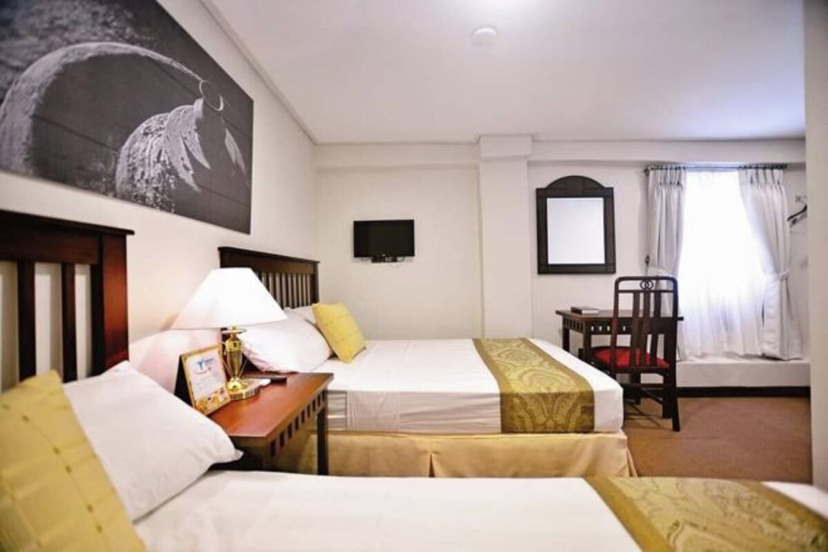 A hotel room with two beds, a desk with a lamp, a television, and a chair.