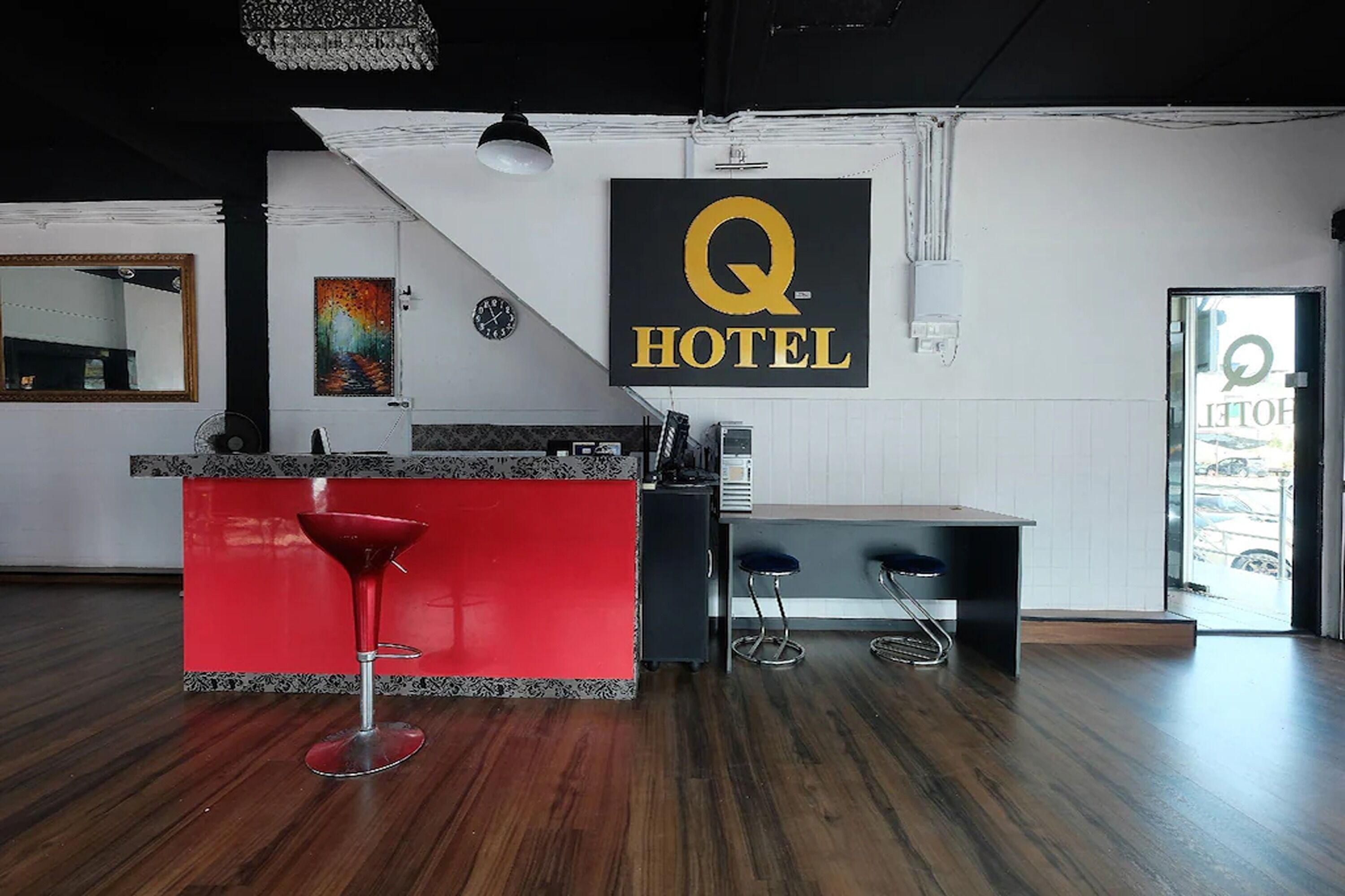 A hotel reception area with a red bar counter, two bar stools, a clock, and a 'Q HOTEL' sign.