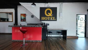 A hotel reception area with a red bar counter, two bar stools, a clock, and a 'Q HOTEL' sign.
