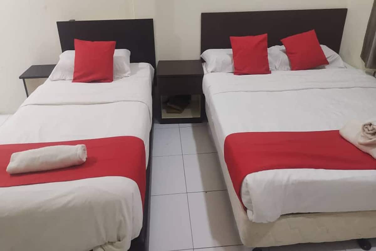Two single beds with red and white bedding, a small nightstand, and a tiled floor.