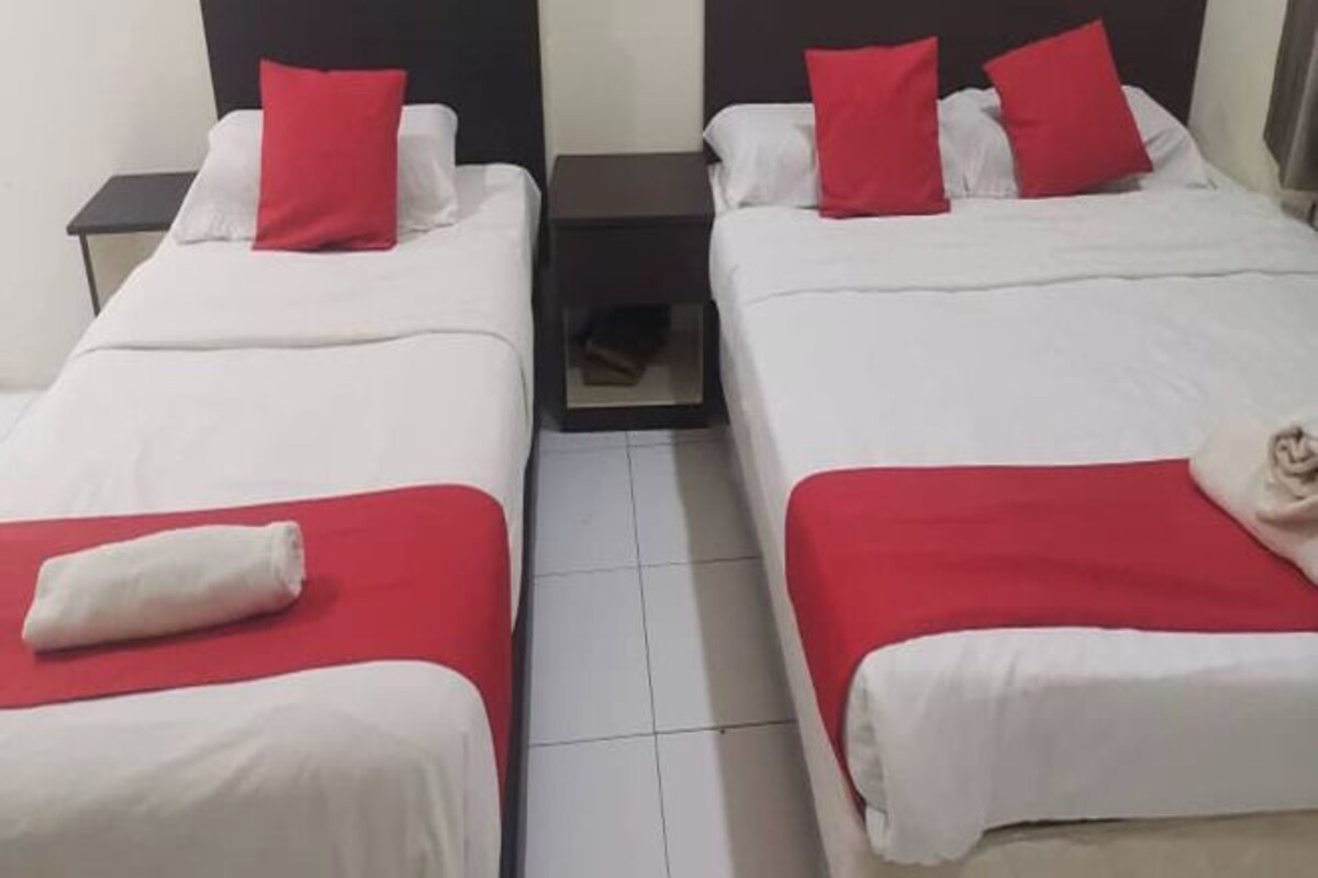 Two single beds with red and white bedding, a small nightstand between them, and a white towel on the floor.