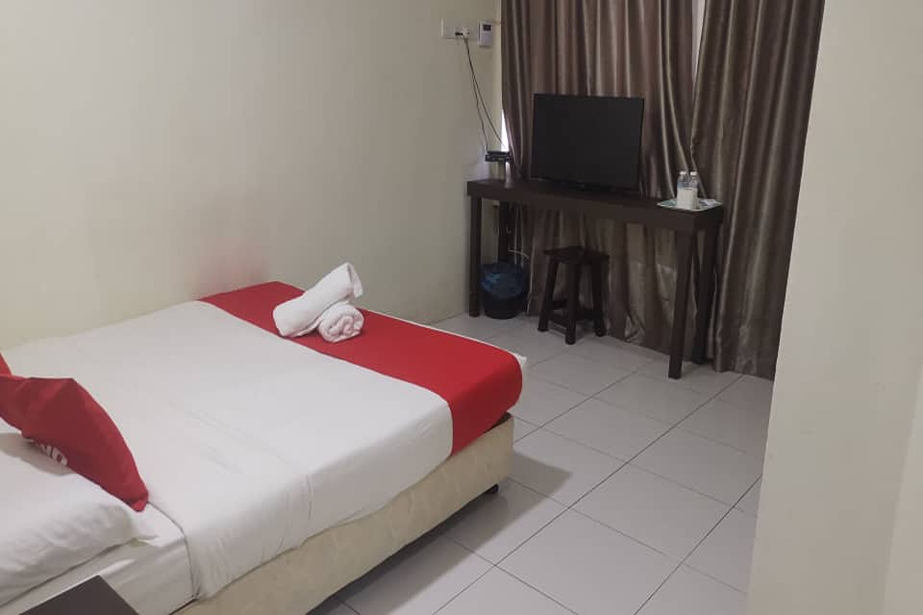 A hotel room with a bed, a TV on a stand, and a desk with a chair.