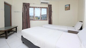 Ein Hotelzimmer mit zwei Betten, einem Fenster mit Vorhängen, einem kleinen Tisch und einem Gemälde an der Wand.