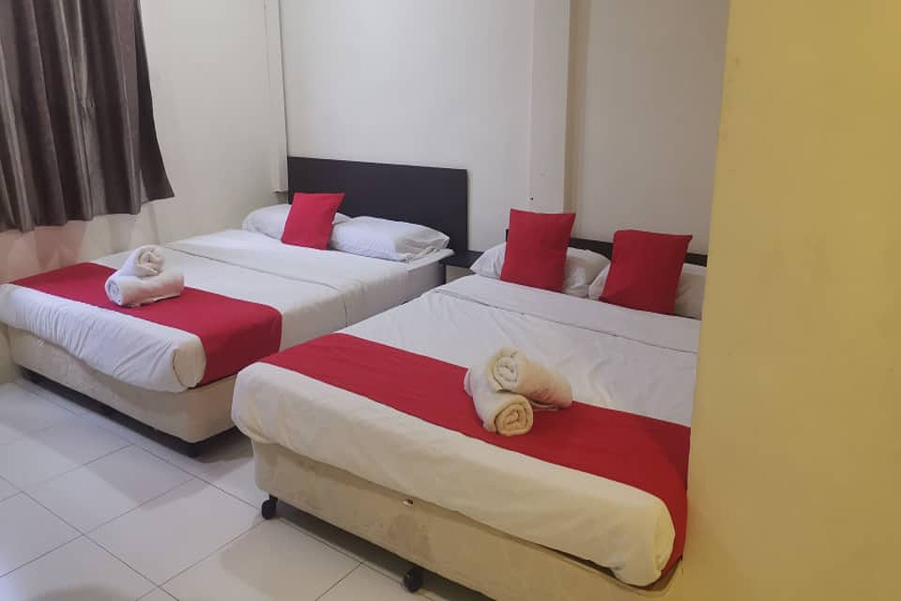 Habitación de hotel con dos camas, cada una con colcha y almohadas rojas y blancas, y una toalla sobre cada cama.