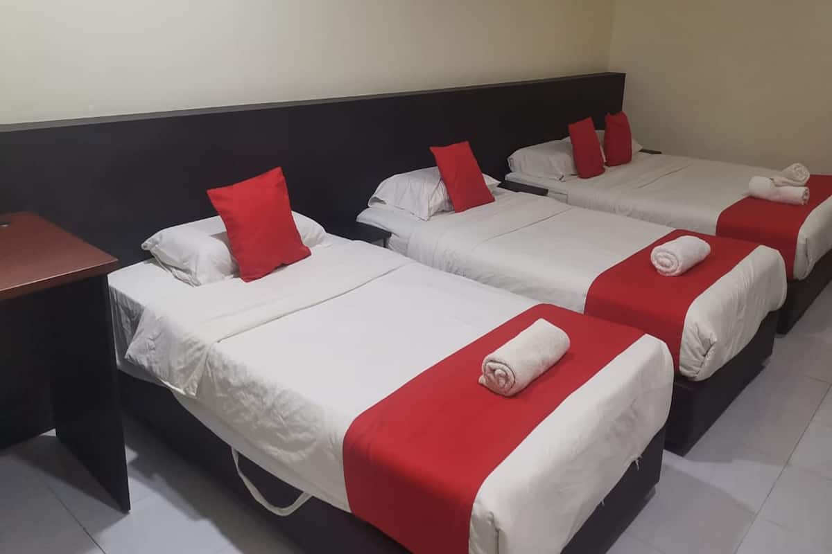 A hotel room with three single beds, each with a red pillow and a rolled towel.