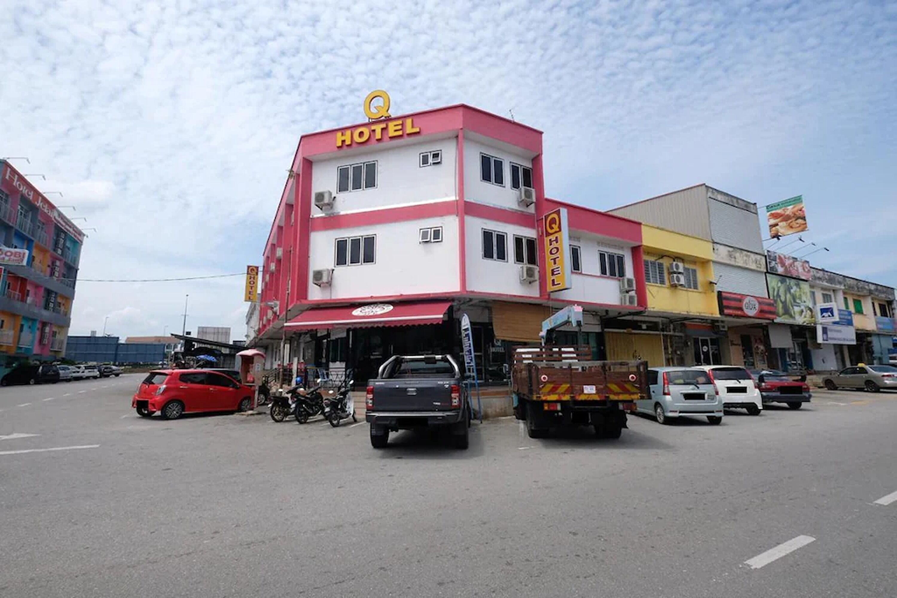 A multi-story hotel with a prominent 'HOTEL' sign on the facade, several parked vehicles, and a clear sky.