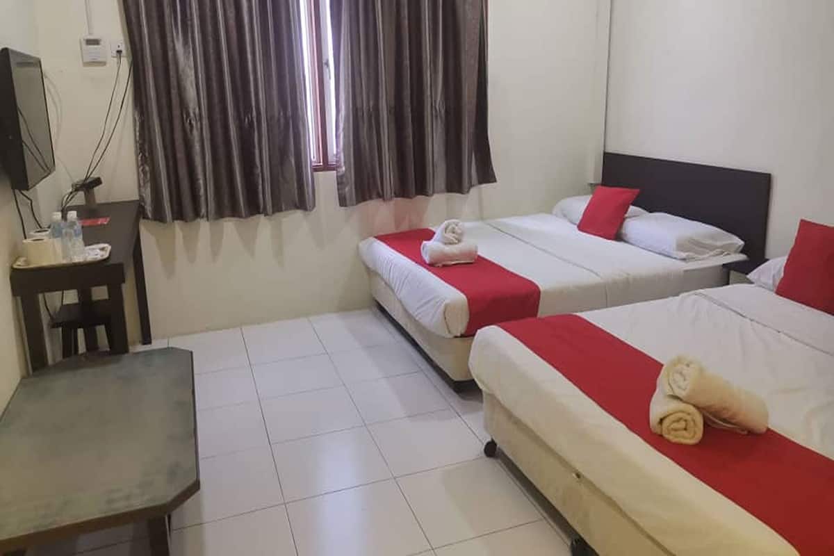 A hotel room with two beds, a desk, a television, and a window with curtains.