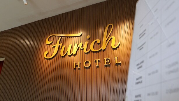 A reception desk with a wooden panel wall and a sign that reads "Furich Hotel".