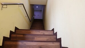 A wooden staircase with metal handrails, leading to a room with a light-colored wall and a ceiling light.