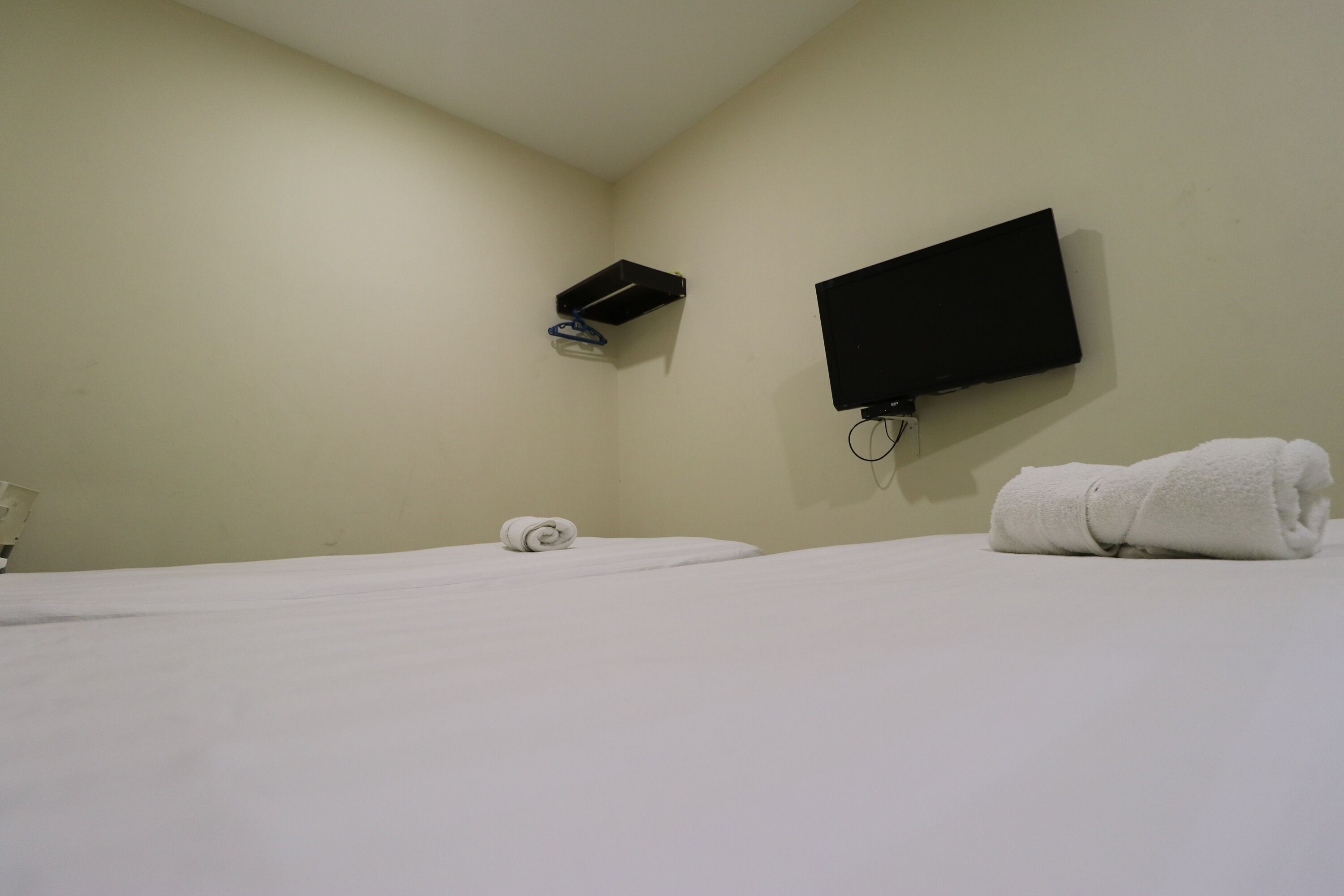A hotel room with a bed, a TV mounted on the wall, and a towel on the bed.