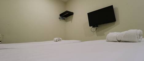 A hotel room with a bed, a TV mounted on the wall, and a towel on the bed.