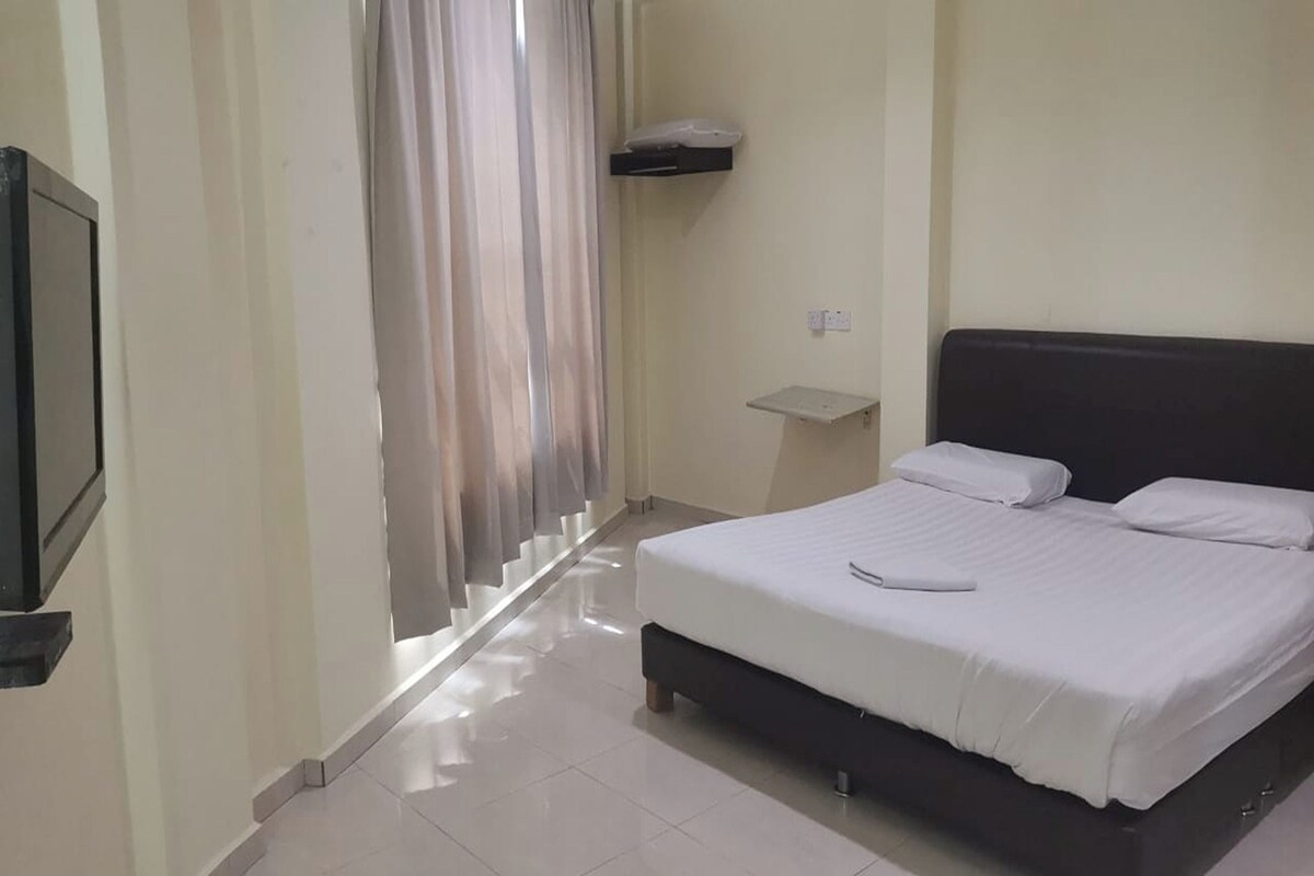 A bedroom with a bed, a bedside table, a TV mounted on the wall, and a curtain.