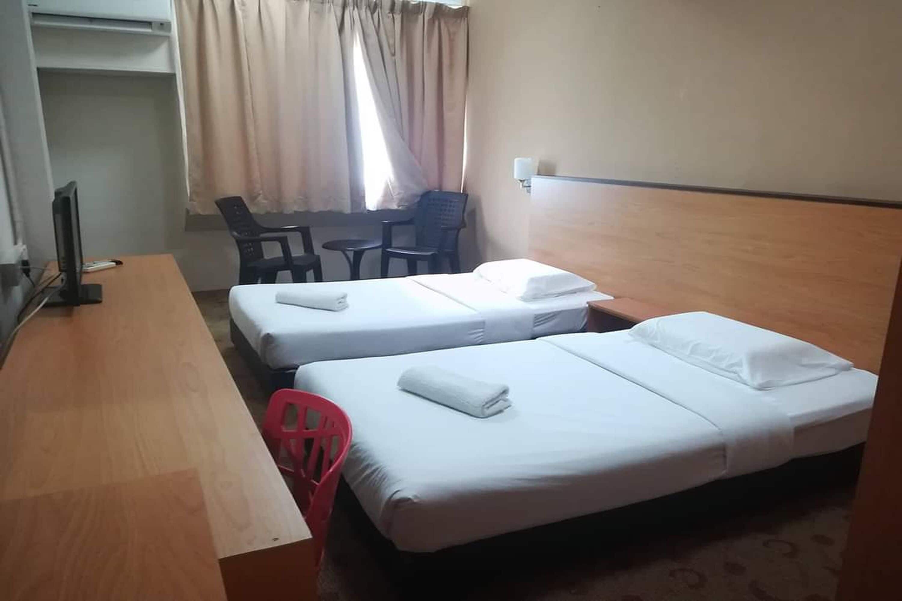 Ett hotellrum med två separata sängar, ett skrivbord, en stol och en TV.