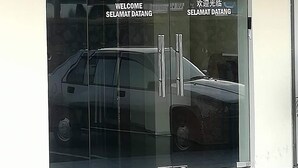 Entrada de un hotel con puerta de cristal, el número 75 y un cartel de bienvenida.