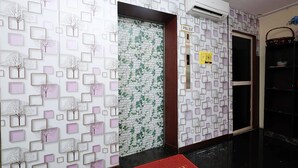 Un pasillo con papel tapiz estampado, una alfombra roja de bienvenida y un cartel con un número de habitación.