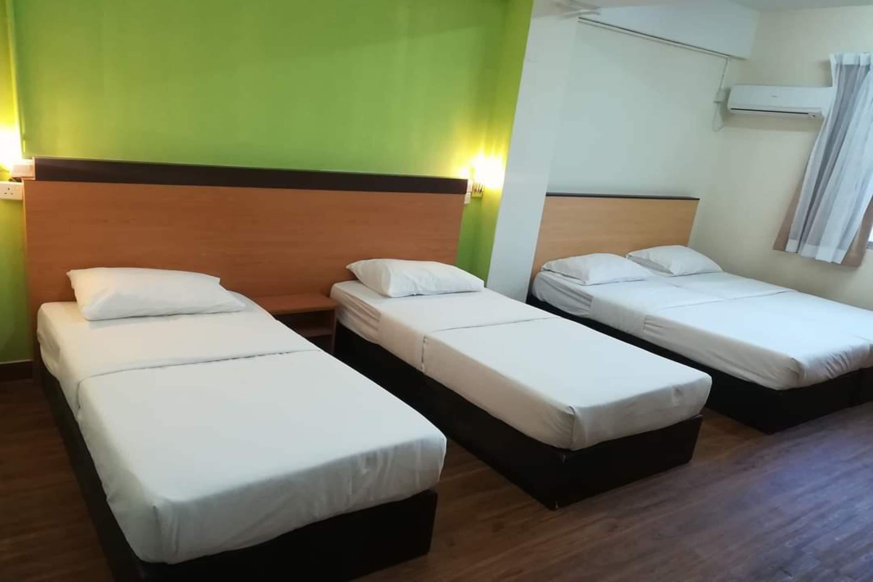Une chambre d’hôtel avec trois lits simples, une tête de lit en bois, un mur d’accent vert et un appareil de climatisation.