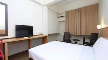 Habitació d'hotel amb un llit, una taula de treball amb televisió, dues cadires, un aire condicionat i una finestra amb cortines.