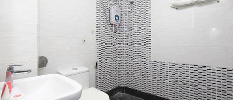 Un baño con lavamanos, inodoro y ducha, con pared revestida de azulejos negros.