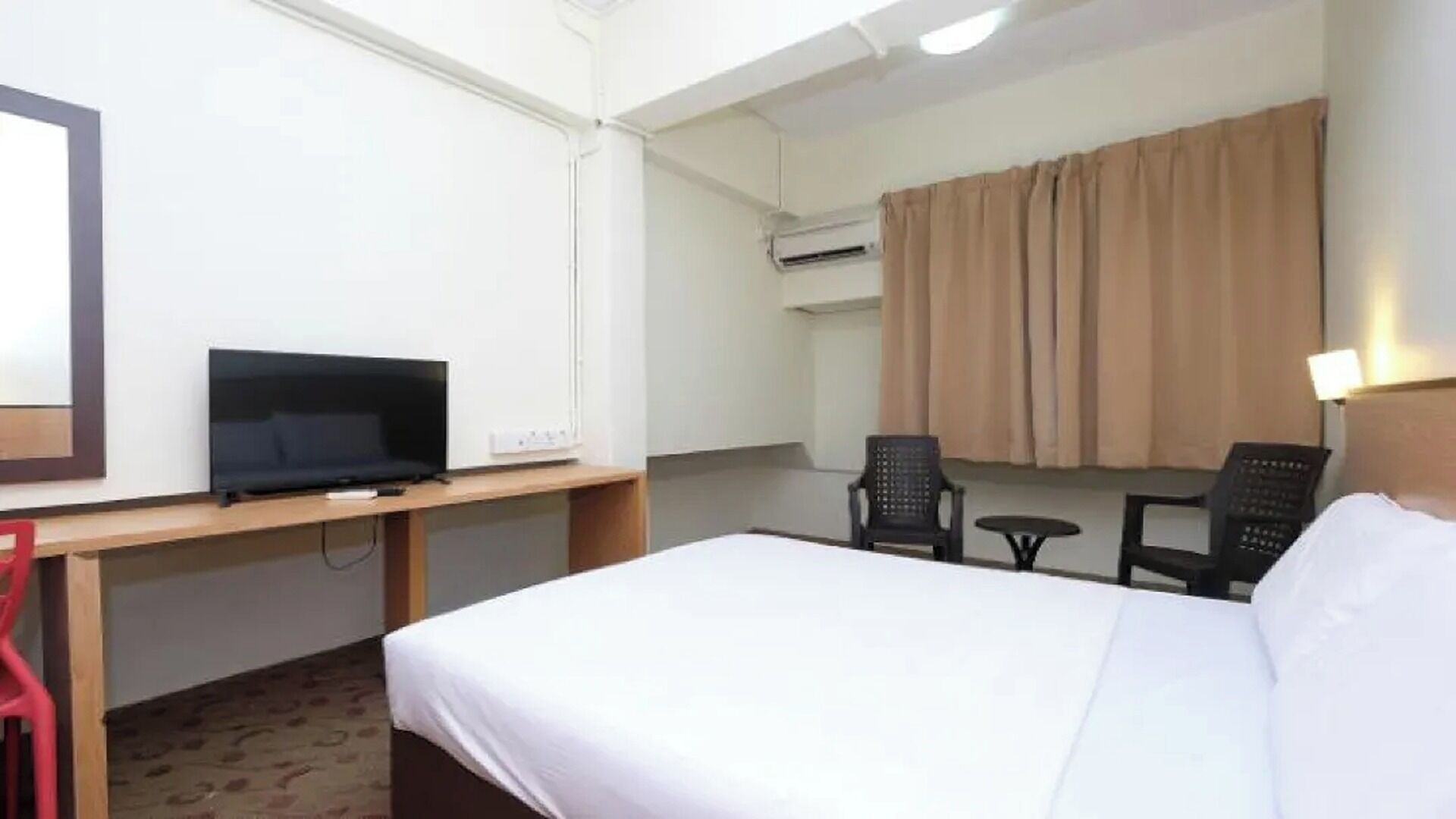 Ein Hotelzimmer mit einem Bett, einem Schreibtisch mit Fernseher, einem Sessel, einem kleinen Tisch und einer Klimaanlage.
